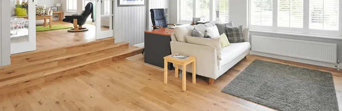 A modern living room with professionally installed laminate flooring, a beige sofa, a small side table, a gray rug, and large windows with white shutters in Philadelphia, PA